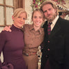 Three people posing together in a festive indoor setting with Christmas decorations.
