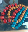 beaded bracelets, one with red and gold beads, the other with blue and gold beads, on a reflective surface.