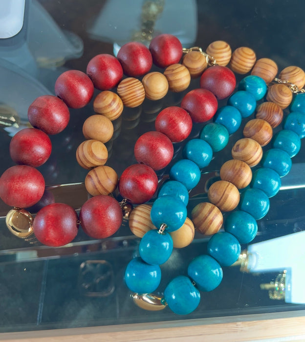 beaded bracelets, one with red and gold beads, the other with blue and gold beads, on a reflective surface.