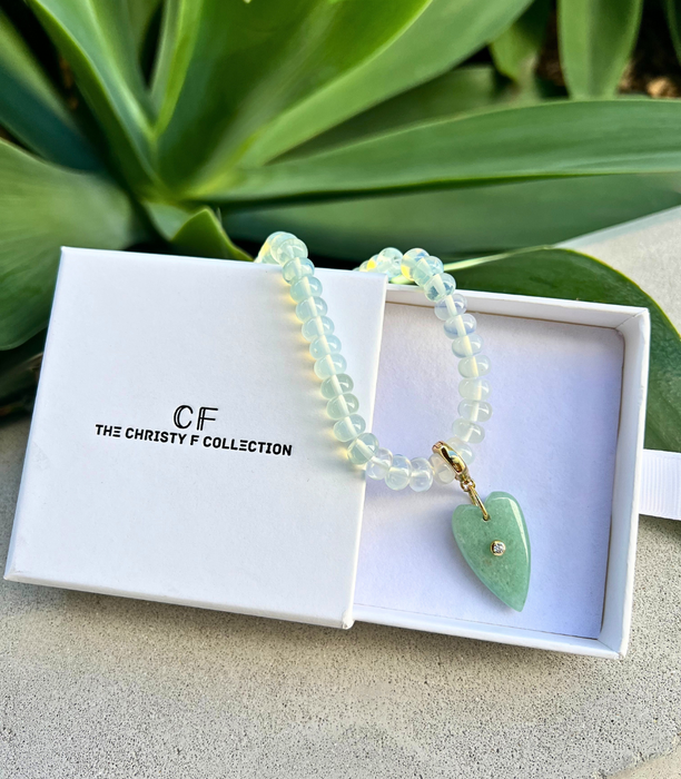 Bracelet with a heart-shaped charm in a 'The Christy F Collection' box with green leaves in the background.