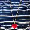 Red heart-shaped pendant on a gold chain against a blue and white striped shirt