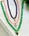 Three beaded necklaces in green, pink, and purple on a textured surface.