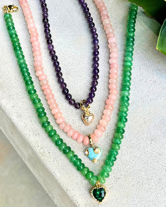 Three beaded necklaces in green, pink, and purple on a textured surface.