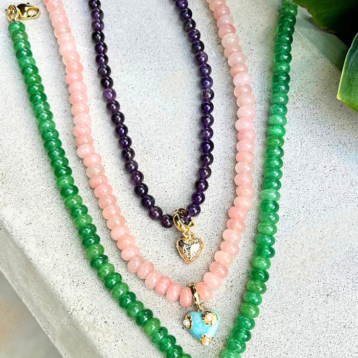 Three beaded necklaces in green, pink, and purple on a textured surface.