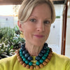 Woman wearing a colorful beaded necklace outdoors with plants in the background