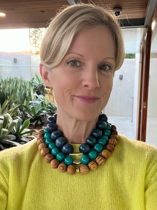 Woman wearing a colorful beaded necklace outdoors with plants in the background