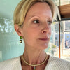 Woman wearing a gold necklace with a green pendant indoors.