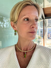 Woman wearing a gold necklace with a green pendant indoors.