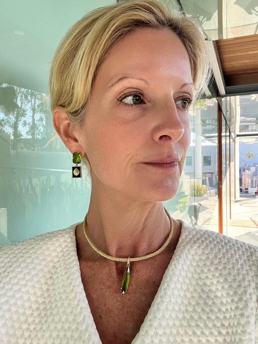 Woman wearing a gold necklace with a green pendant indoors.