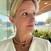 Woman wearing a white textured garment with a necklace, standing outdoors.