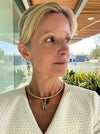 Woman wearing a white textured garment with a necklace, standing outdoors.