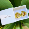 Gold earrings in a white box with 'CF' branding on a green leafy background