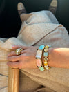 Close-up of a hand wearing multiple bracelets and rings on a neutral background