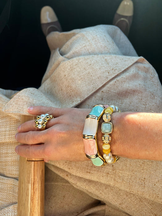 Close-up of a hand wearing multiple bracelets and rings on a neutral background