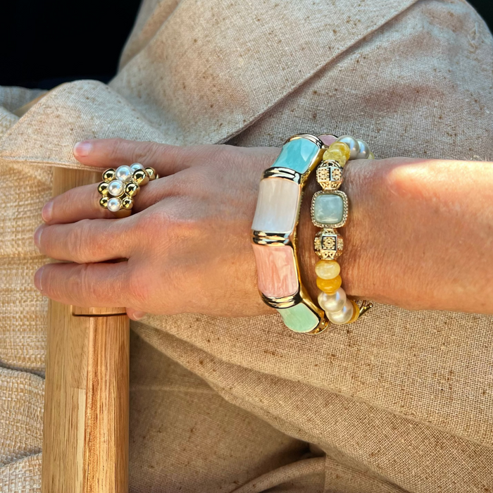 Close-up of a hand wearing multiple bracelets and rings on a neutral background