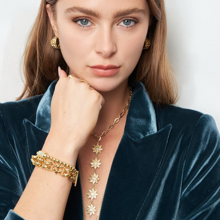 Woman wearing gold jewelry including a necklace, bracelet, and earrings on a white background