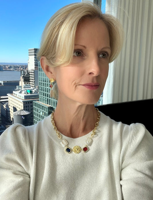 A person wearing a white sweater and a necklace with a gold chain and pearl elements.