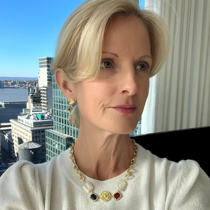 A person wearing a white sweater and a necklace with a gold chain and pearl elements.
