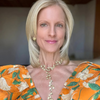 Woman wearing an orange floral dress with a gold necklace indoors