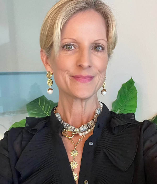 Woman wearing a black outfit with gold jewelry, blue ceramic jewelry and pearl jewelry in front of green leaves