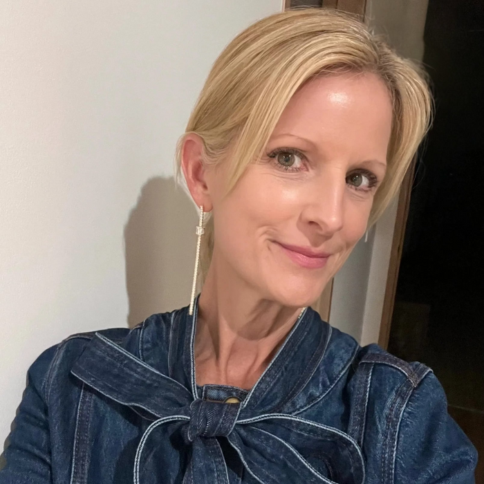 Woman wearing a blue denim jacket with a large bow tie, indoors.