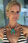 Woman wearing a striped top and turquoise necklace with a blurred outdoor background