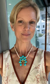Woman wearing a floral top and turquoise necklace indoors