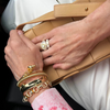 Close-up of hands with gold jewelry holding a beige clutch.