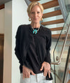 Woman wearing a black cardigan with a turquoise necklace in an indoor setting.