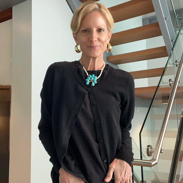 Woman wearing a black cardigan with a turquoise necklace in an indoor setting.