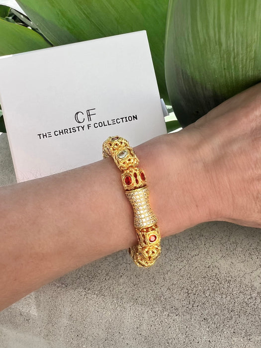 Gold bracelet with red stones on a wrist, with 'The Christy F Collection' card in the background.