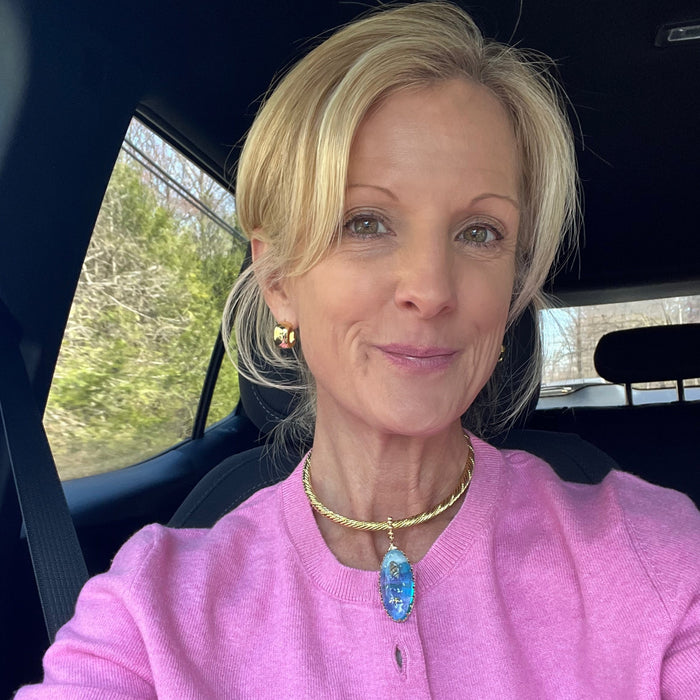 Woman in a pink cardigan sitting inside a vehicle with a blurred outdoor background