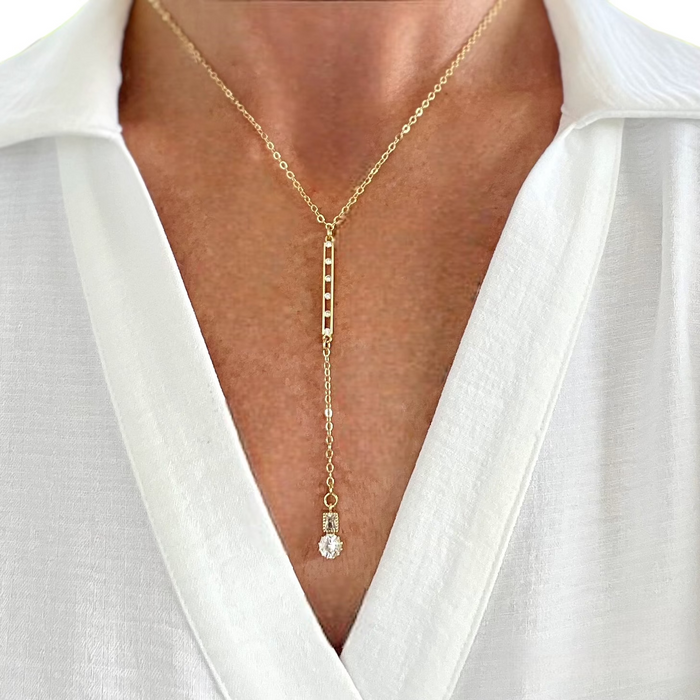 Gold necklace with a pendant on a person wearing a white shirt.