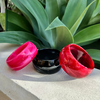 Three colorful lip-shaped bangles on a concrete surface with green leaves in the background
