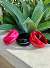 Three colorful lip-shaped bangles on a concrete surface with green leaves in the background