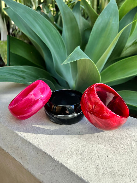 Three colorful lip-shaped bangles on a concrete surface with green leaves in the background