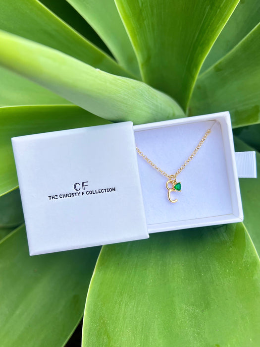 Gold necklace with a green pendant in a white box on a green leafy background