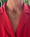 Gold necklace with a green pendant worn by a person in a red shirt against a blurred green background