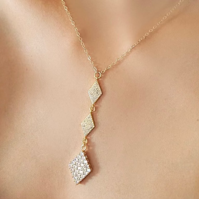 Gold necklace with diamond-shaped pendant on a person's neck