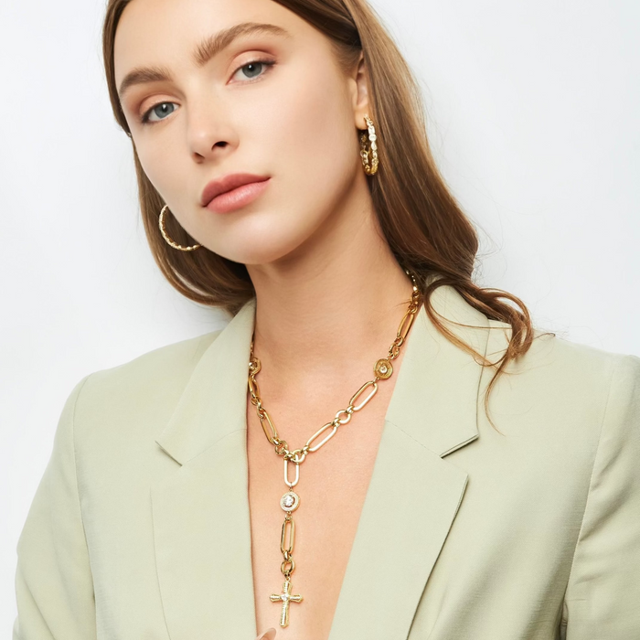 Woman wearing gold jewelry including a necklace, earrings, and ring on a light background