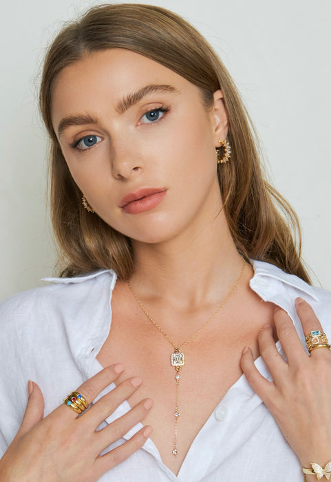 Woman wearing gold jewelry including a necklace, earrings, and rings on a plain background