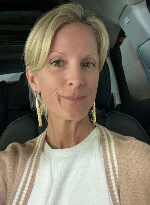 Woman sitting inside a vehicle wearing a beige cardigan and white top.
