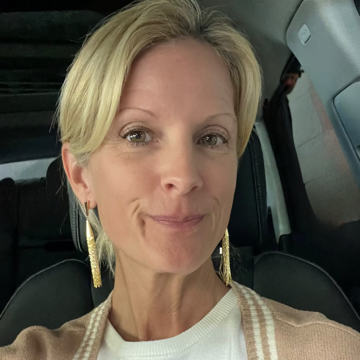 Woman sitting inside a vehicle wearing a beige cardigan and white top.