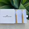 Gold tassel earrings in a white box with 'CF The Christy F Collection' branding, against a green leafy background.