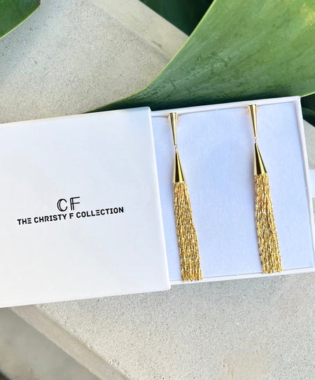 Gold earrings in a 'The Christy F Collection' box with green leaves in the background