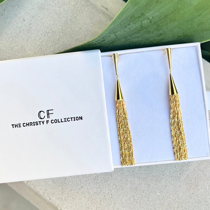 Gold earrings in a 'The Christy F Collection' box with green leaves in the background