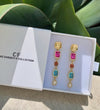 Colorful earrings in a Christy F Collection box with green leaves in the background