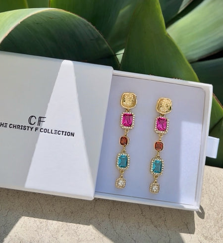 Colorful earrings in a Christy F Collection box with green leaves in the background