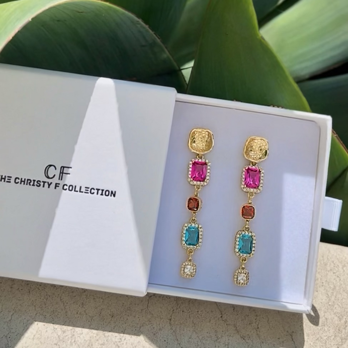 Colorful earrings in a Christy F Collection box with green leaves in the background