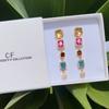 Colorful earrings in a white box with 'CF' branding, set against a green leafy background.